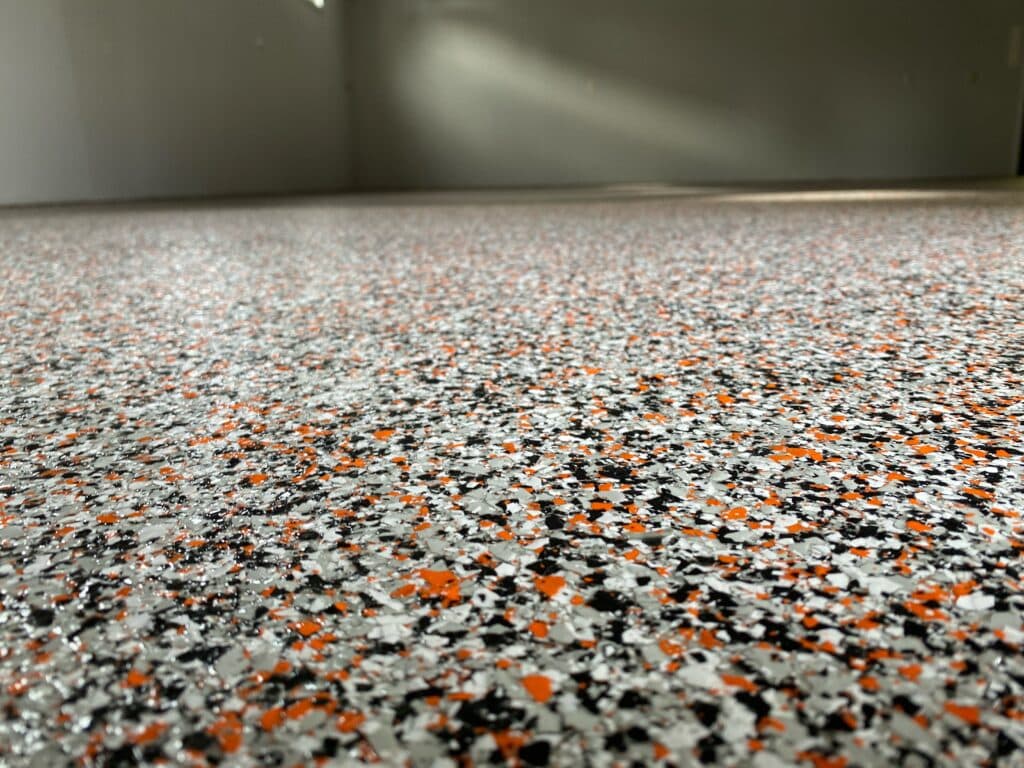 This is an image of a speckled floor with grey, black, and orange colors. Light shines on the surface, and the walls meet in the corner.